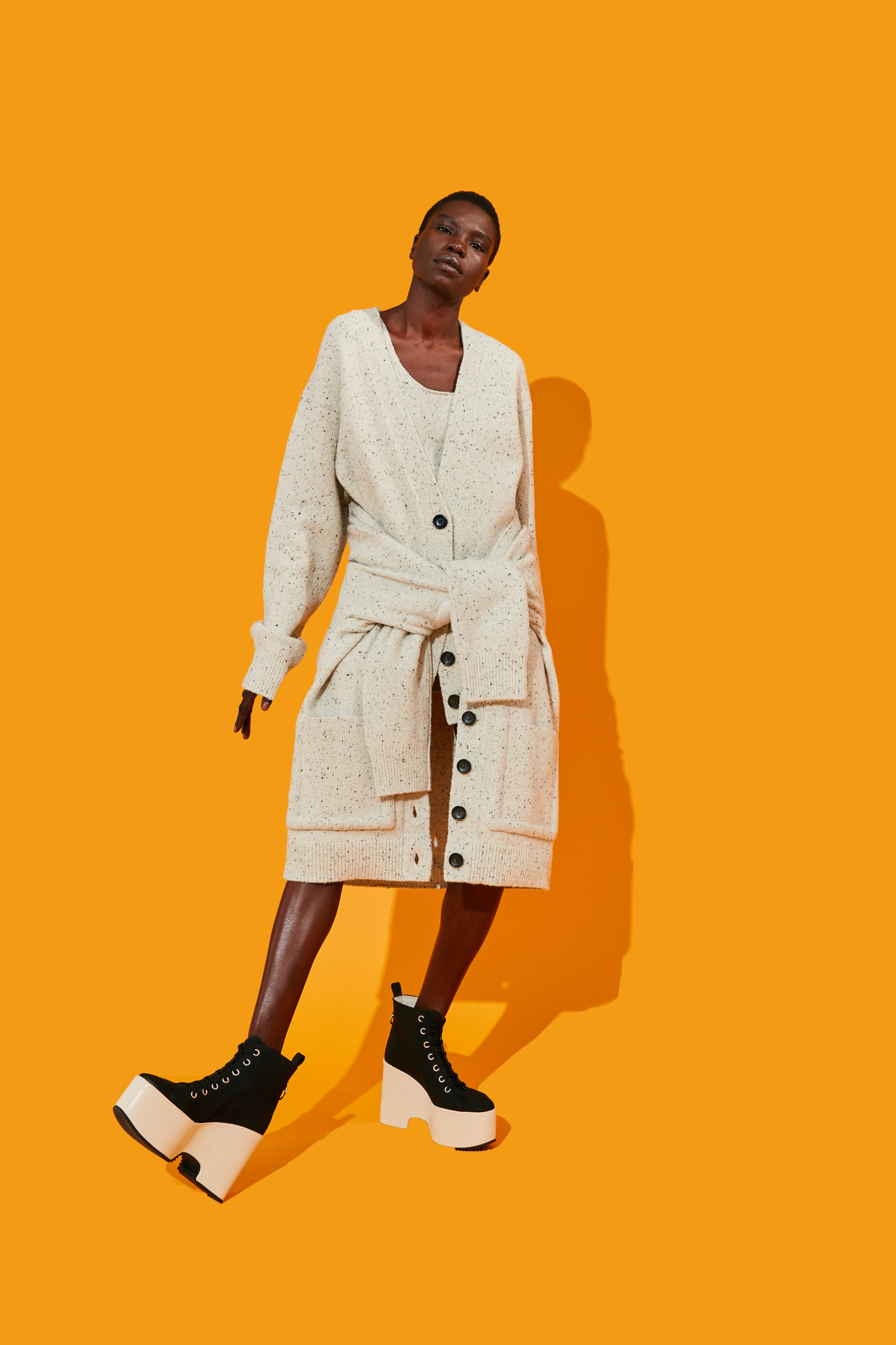 Model wearing a stylish sweater dress and platform boots against an orange background.