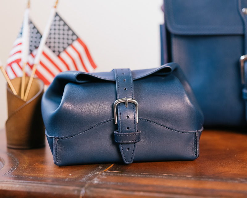 A navy leather bag with a buckle on a table.