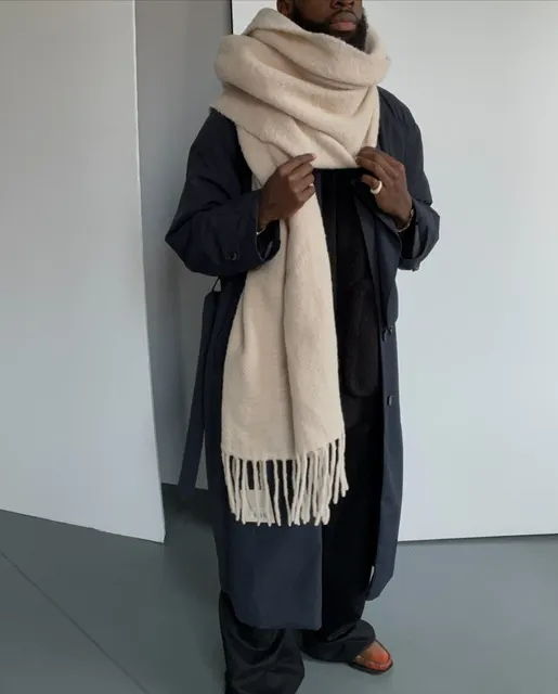 Person wearing a long coat and a beige scarf, standing indoors.