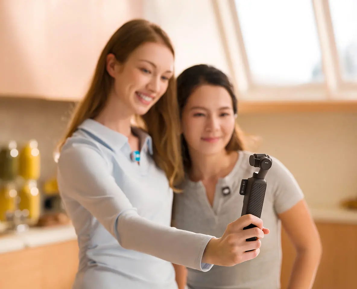 Two women taking a selfie with a DJI Osmo Pocket 4 in a kitchen.