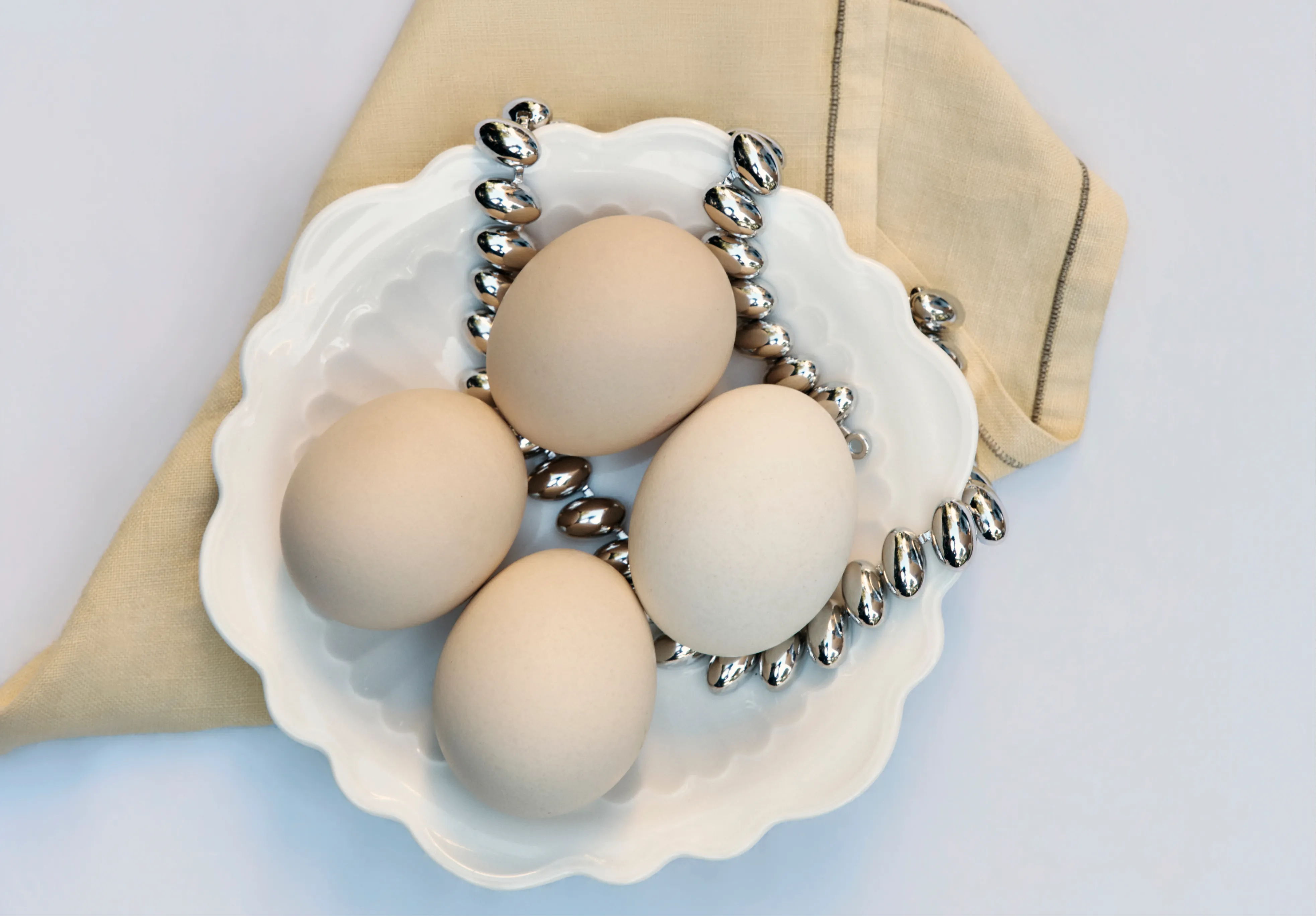 Four eggs in a white bowl with a silver chain and a beige napkin.