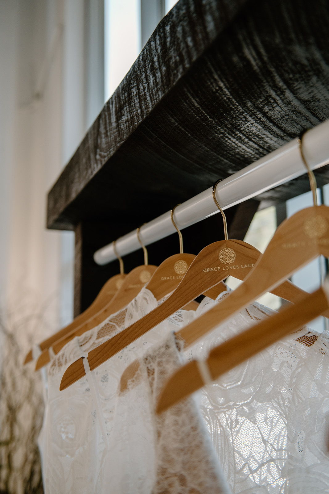 White lace garments hanging on wooden hangers against a dark wooden shelf.