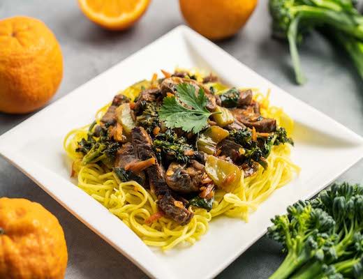 Plate of noodles topped with vegetables and garnished with cilantro, surrounded by oranges.