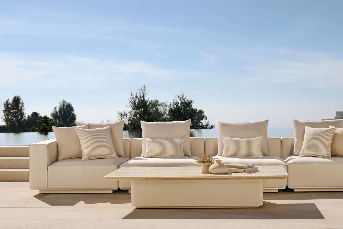 Modern white outdoor sofa with neutral cushions and a matching coffee table on a terrace overlooking water and open sky.