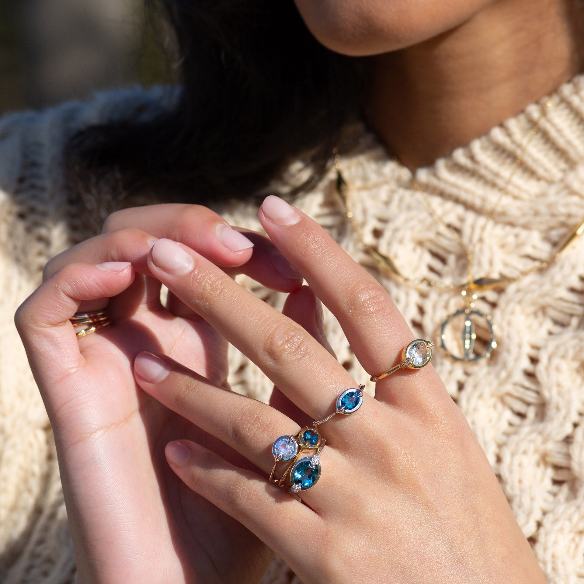 Close-up of hands wearing multiple rings against a knitted sweater background.