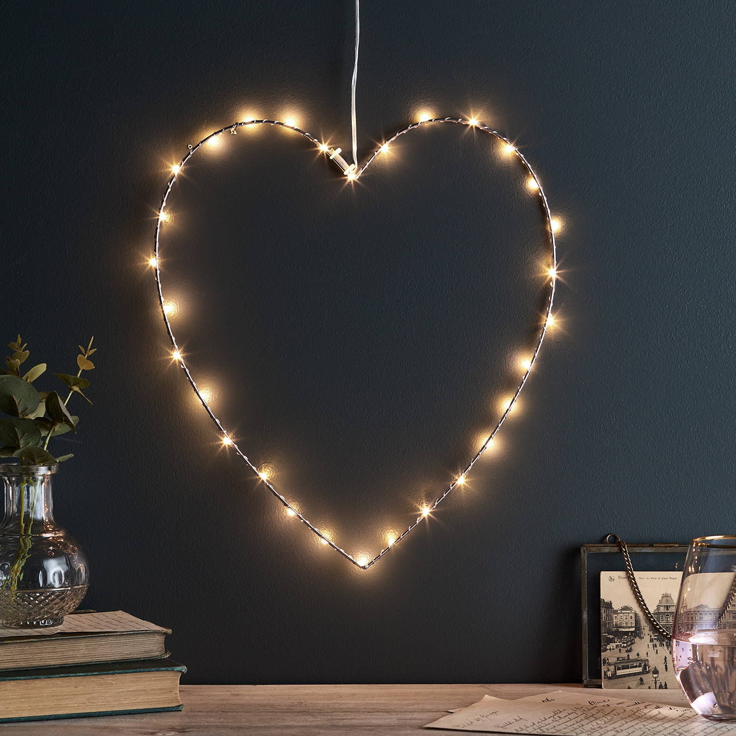 A rose gold heart light on a black wall above a mantlepiece.
