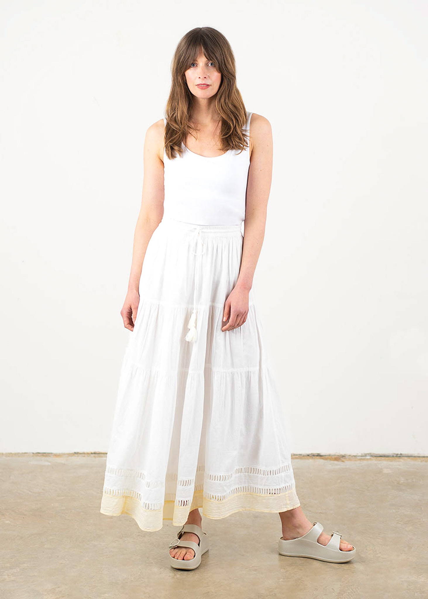 A model wearing a white sleeveless vest with a long white maxi skirt with tiered detail and a yellow panel at the hem and off white platform slides.