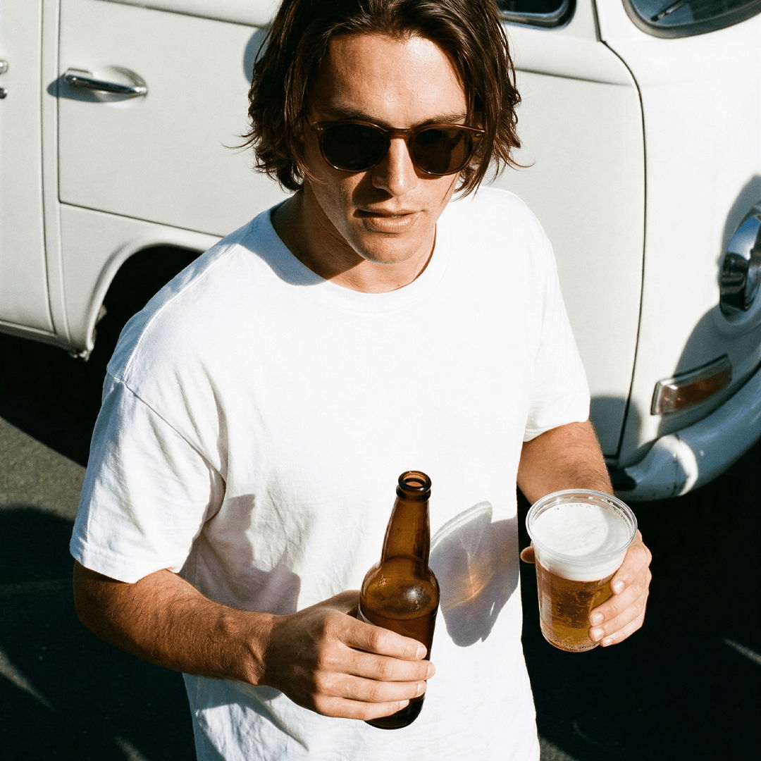 Man in sunglasses holding a beer bottle and a cup of beer.