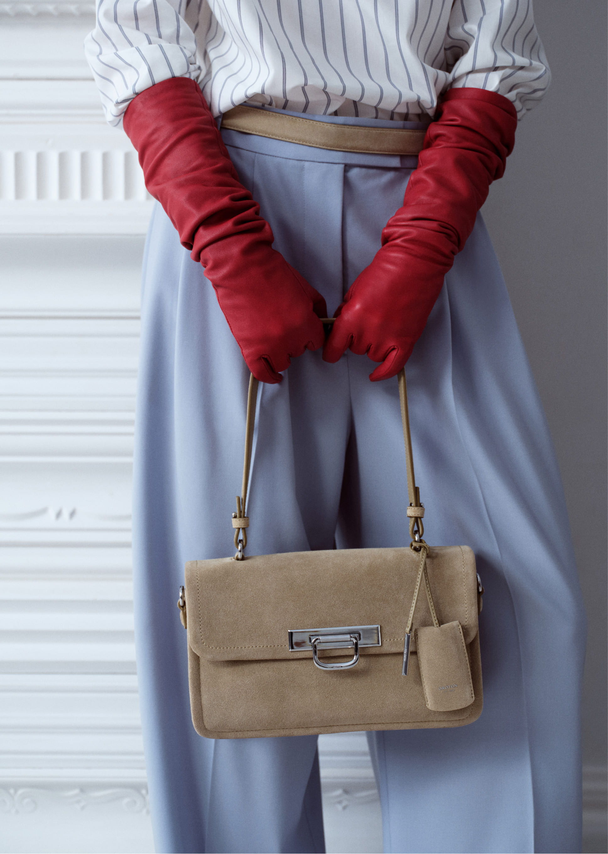 A person wearing red gloves holding a beige handbag, with light blue pants.