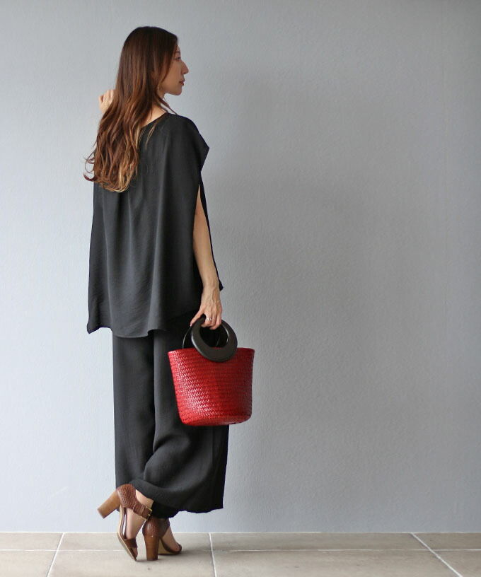 Woman in black outfit holding a red bag, facing a gray wall.