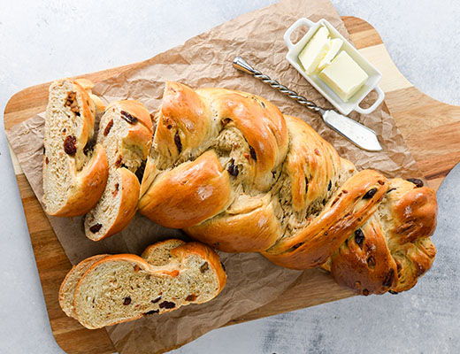 Braided bread loaf with butter on a wooden cutting board.
