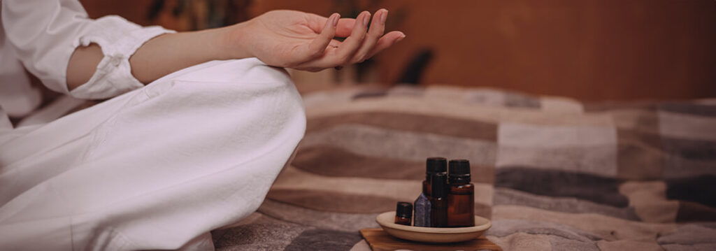 A person meditating with essential oils on a small table.