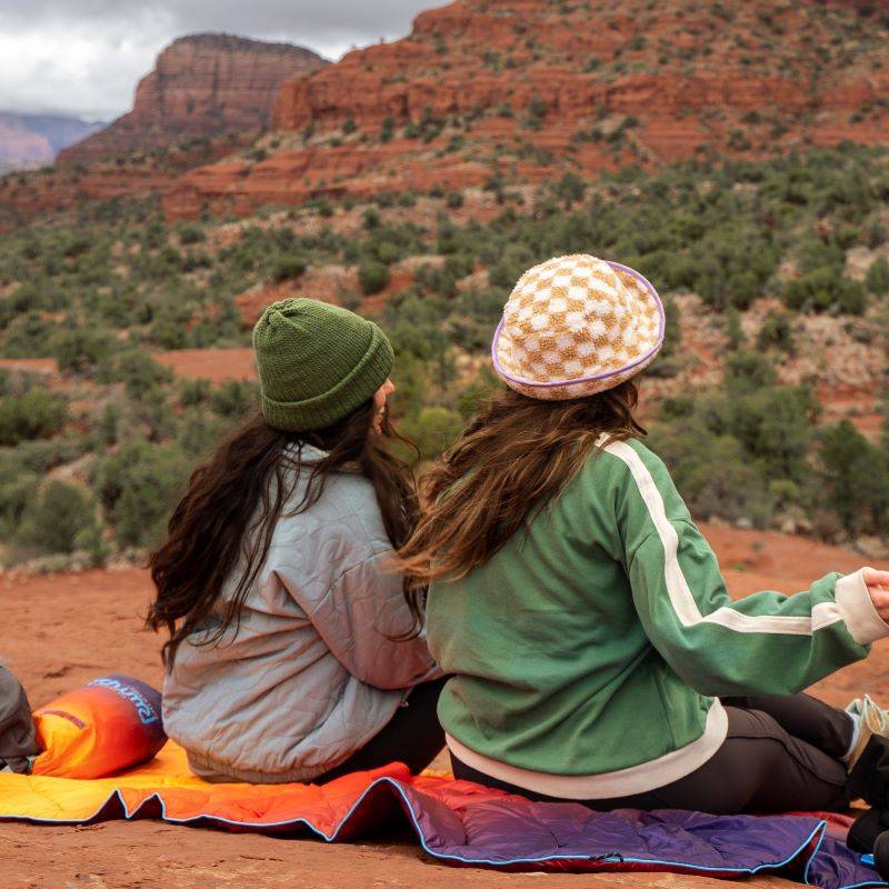 Two women sitting on a blanket in the outdoors