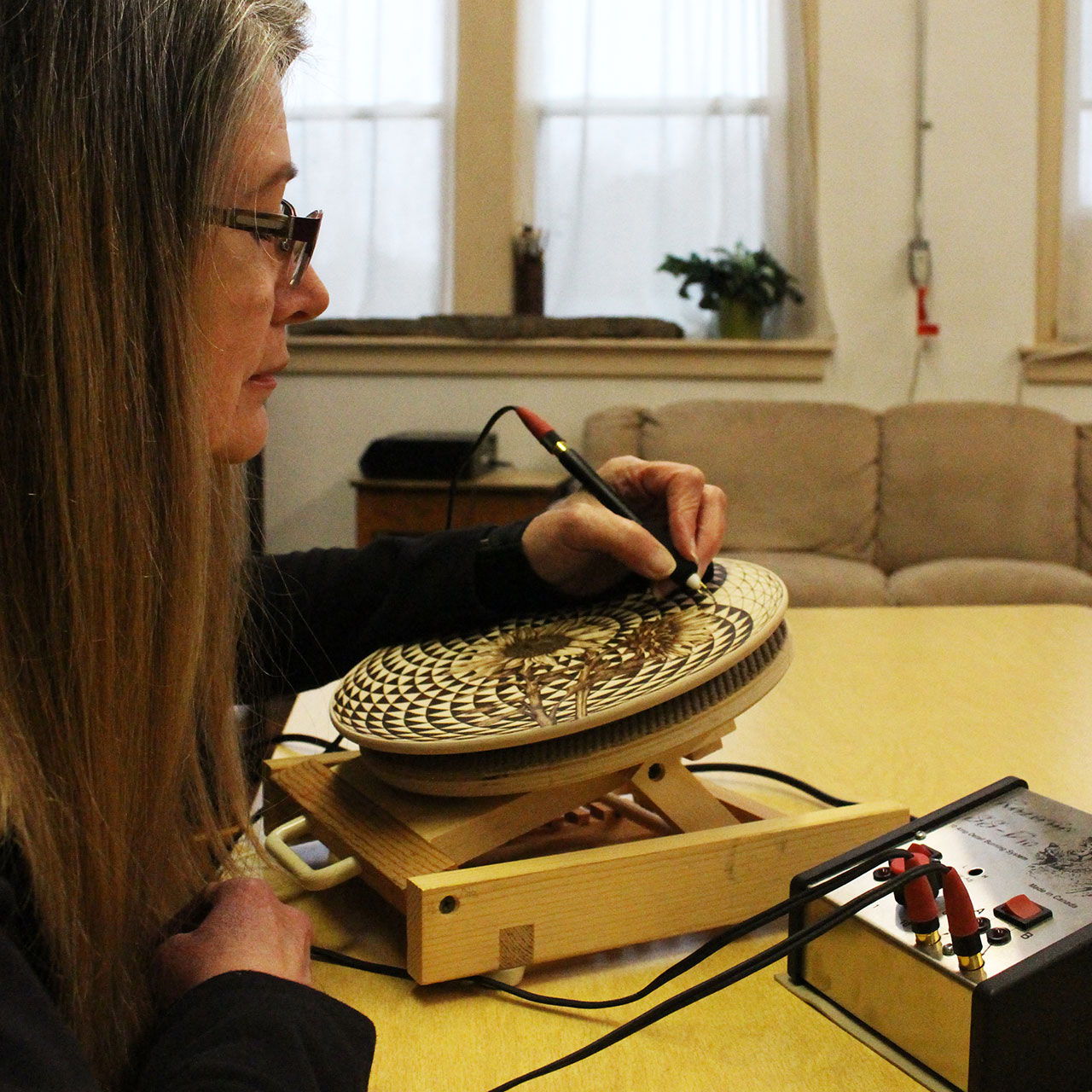 Woman using a tool on a patterned wooden surface at a table.