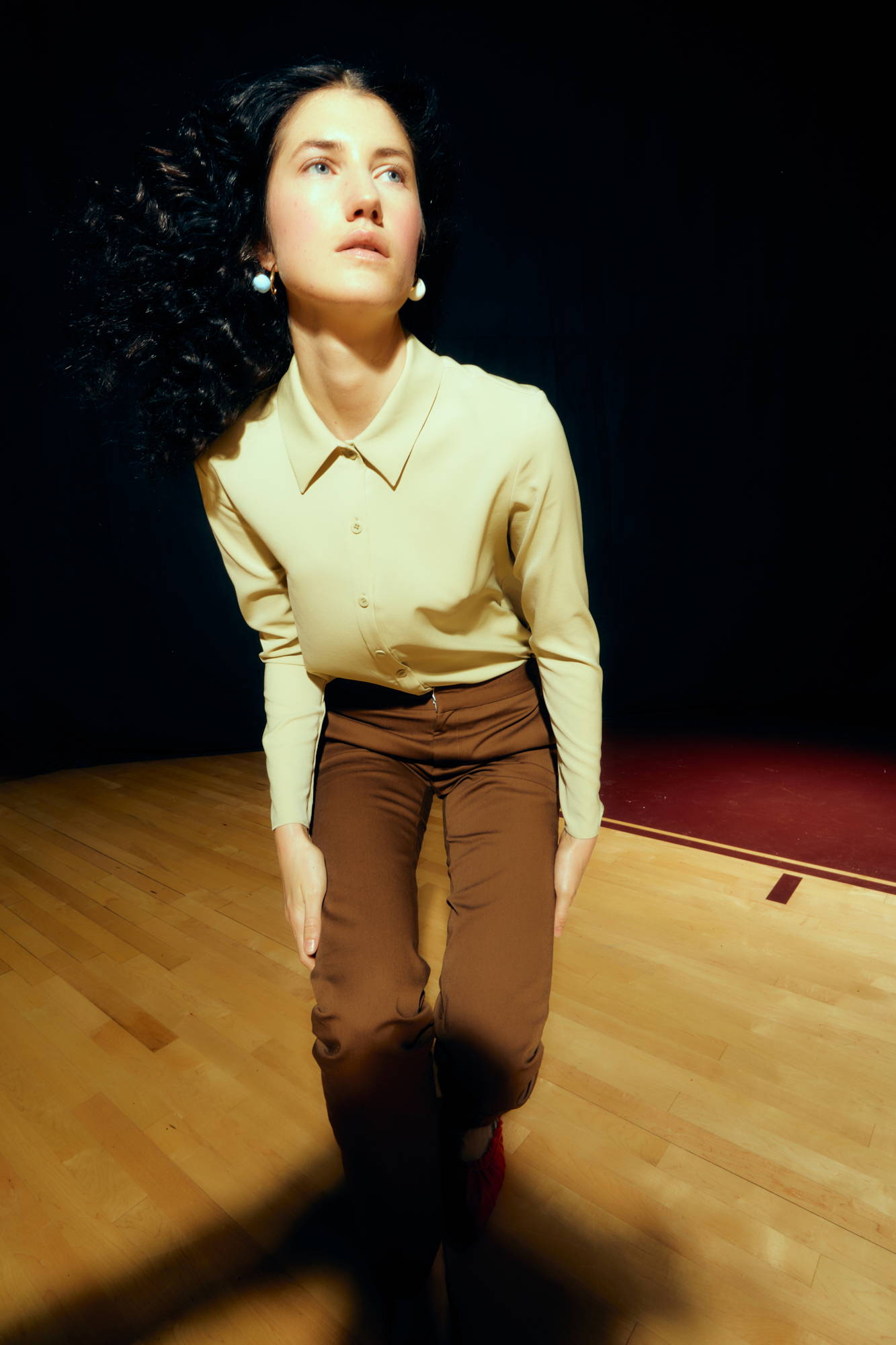 A person in a beige shirt kneels on a wooden floor.
