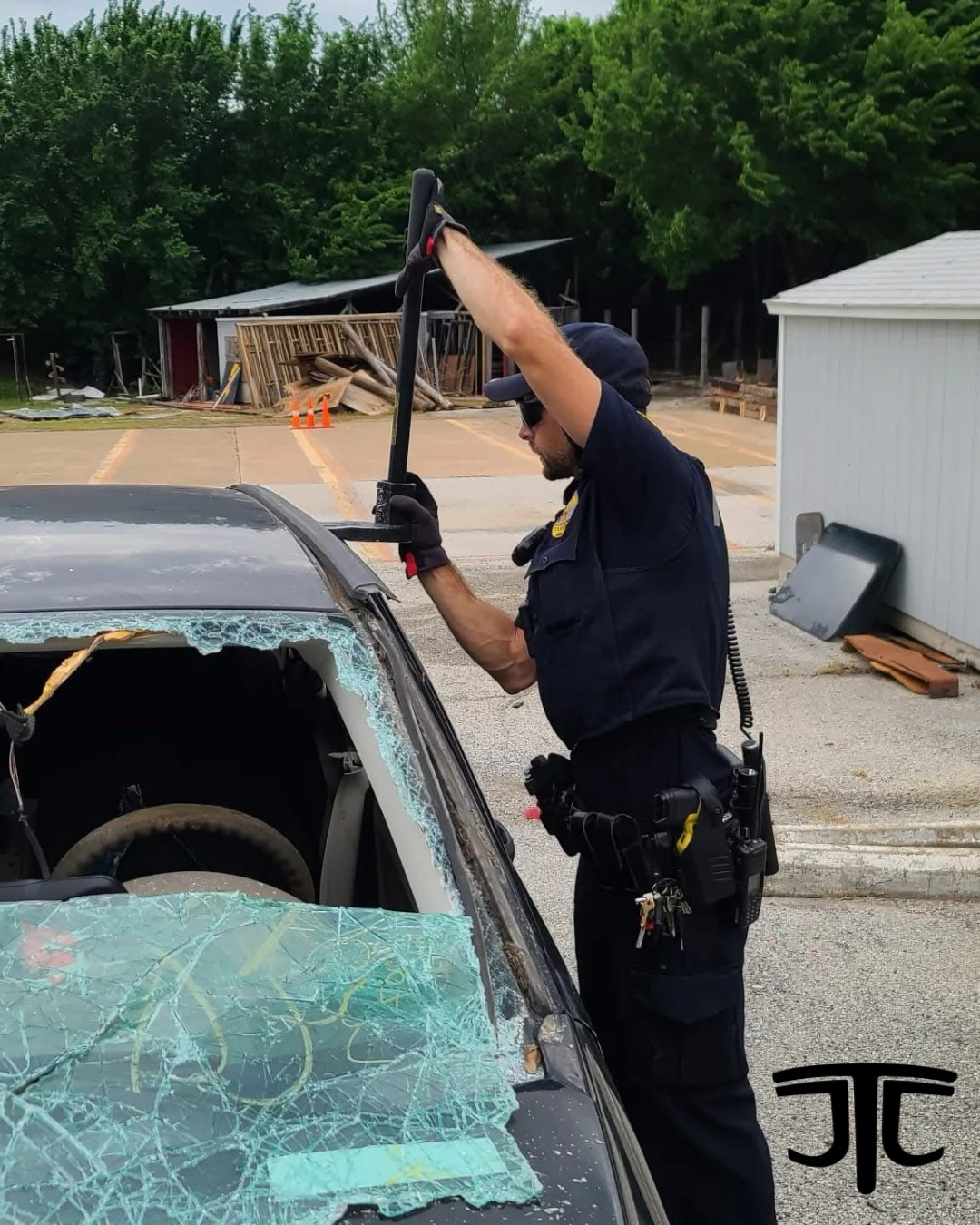 Police officer breaking a car window with a tool in a parking lot.