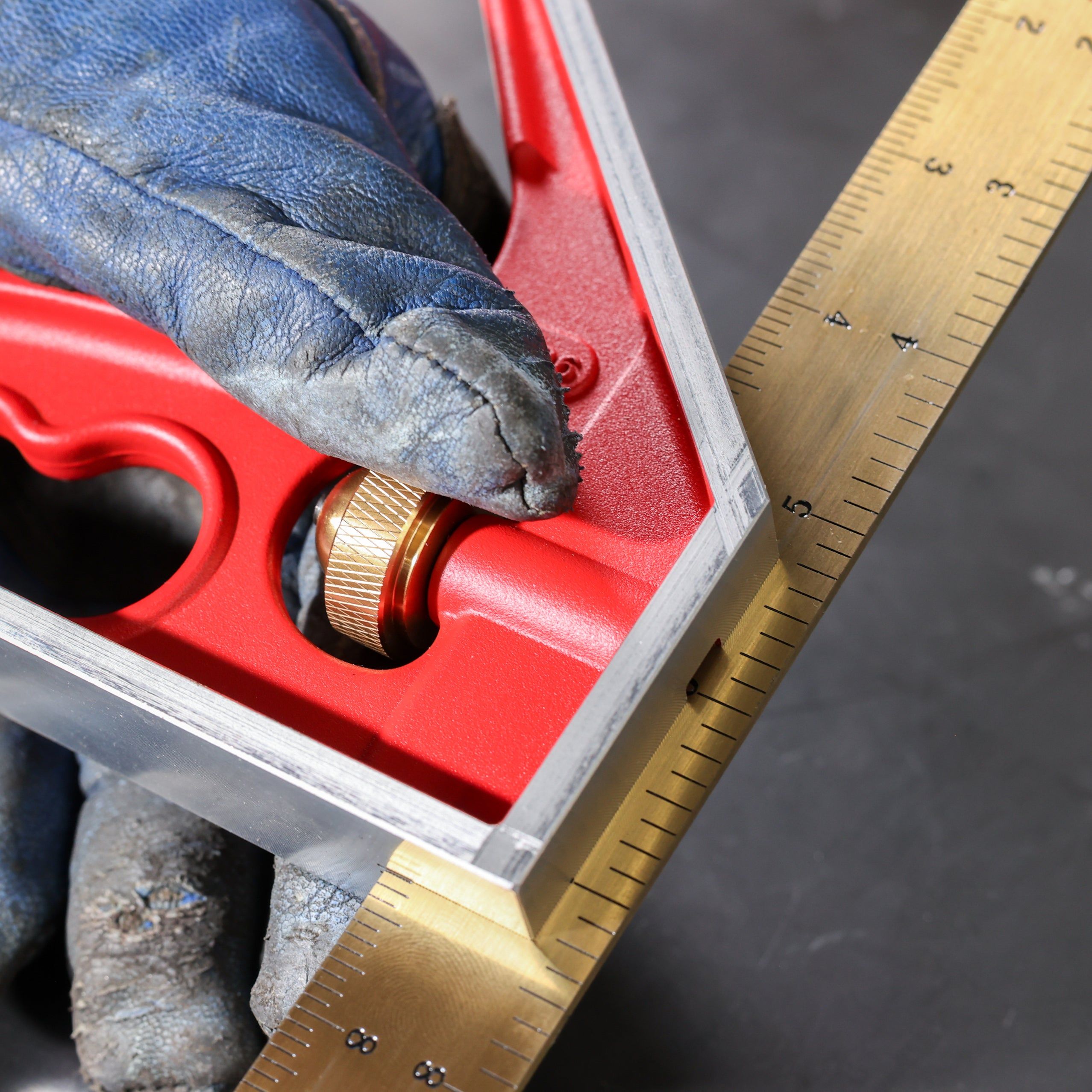 Hand holding a red square tool against a measuring ruler.