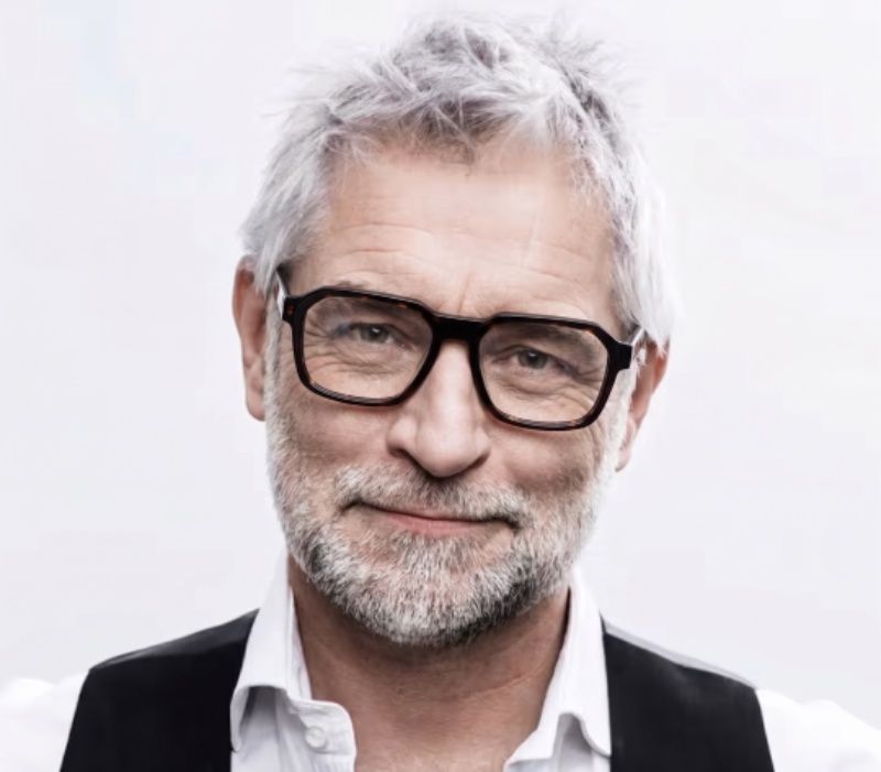 man with grey hair wearing Kaya, thick black squared eyeglasses, on a white background