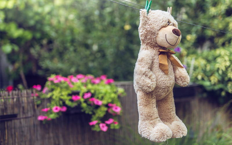Een knuffelbeer is wegens huisstofmijtallergie zojuist gewassen en hangt buiten aan de waslijn te drogen.