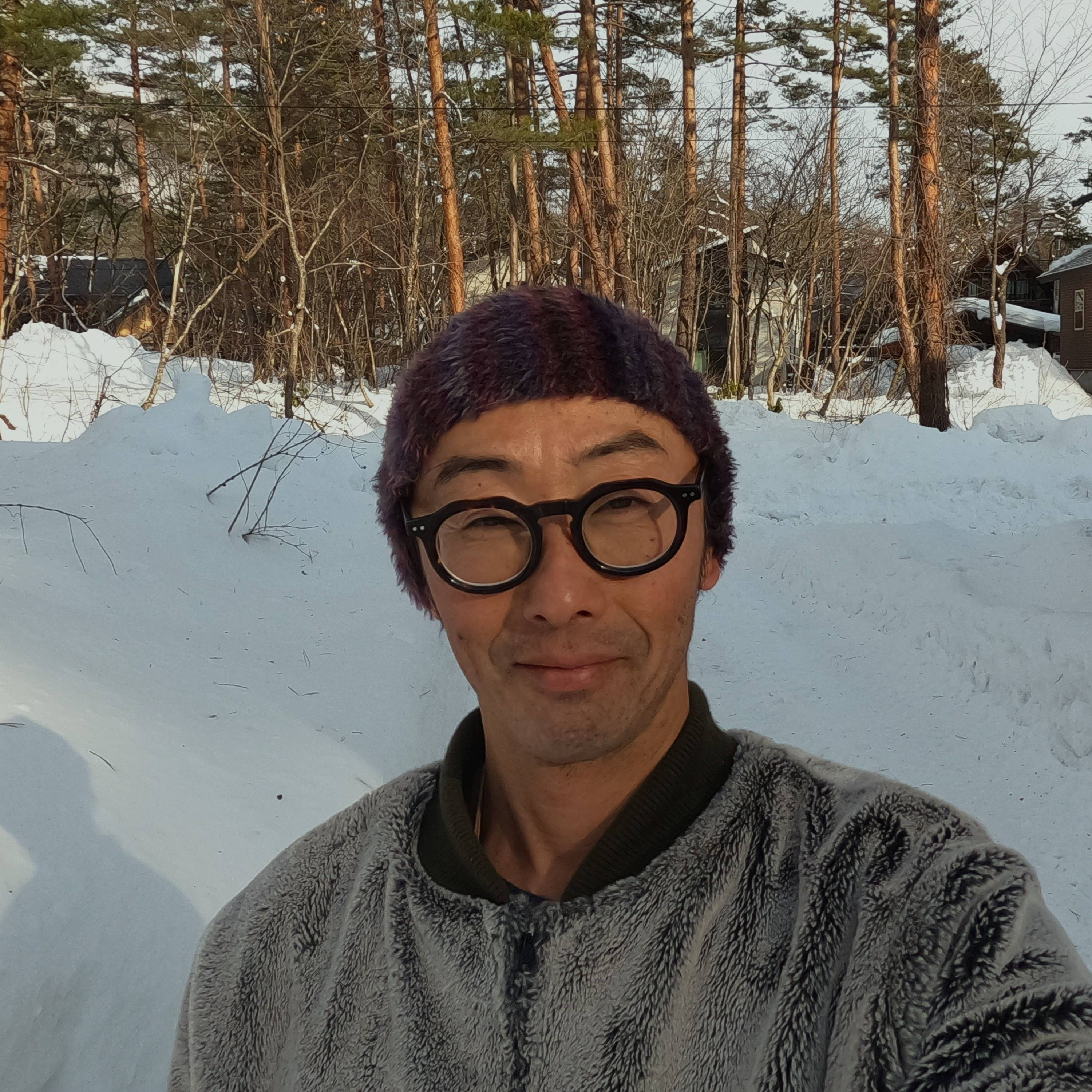 A person in winter clothing standing in a snowy landscape with trees.