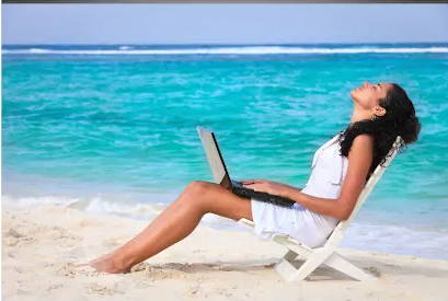 Woman on beach sunbathing while working on her computer.