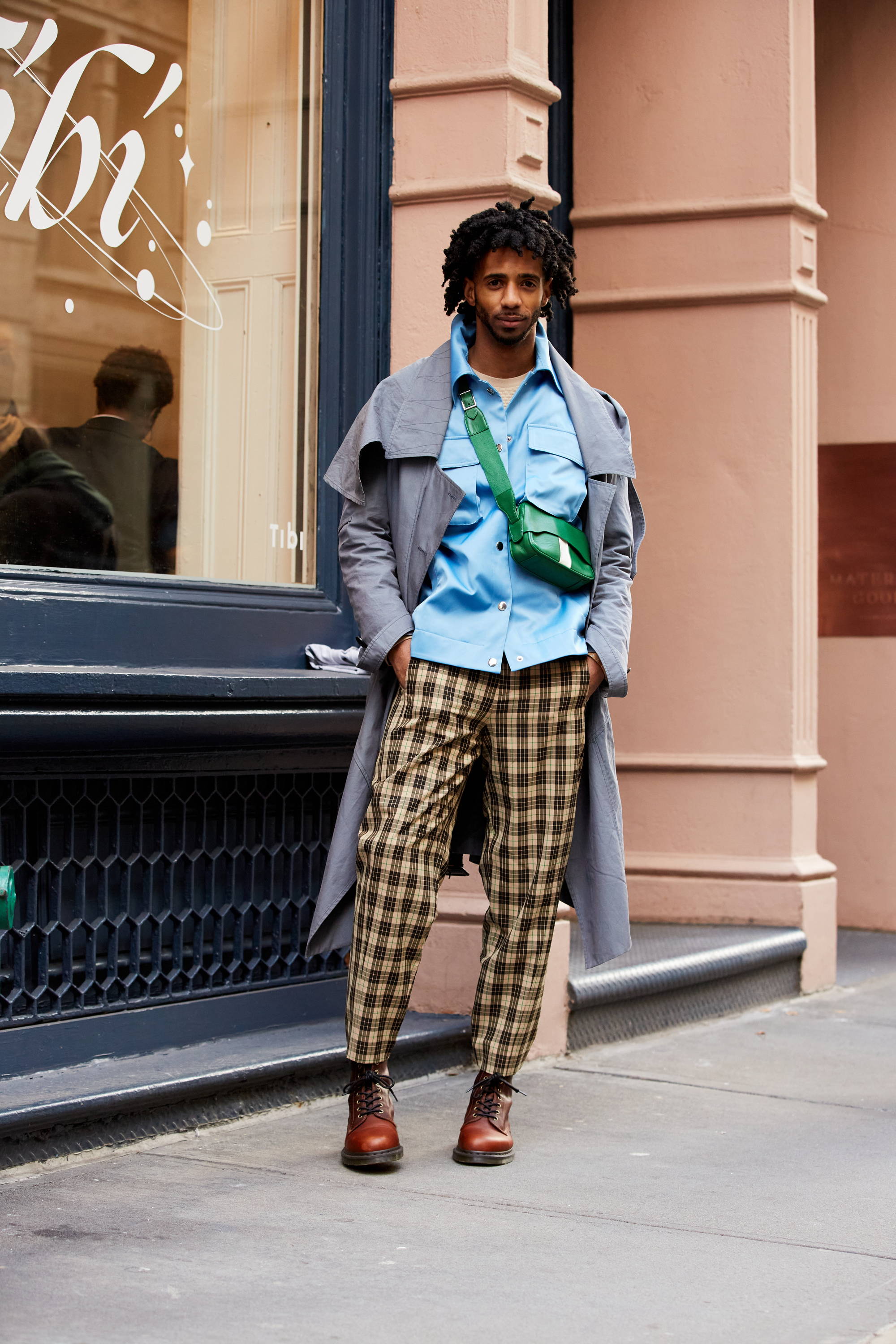 Person in stylish outfit standing outside a store with a modern facade.