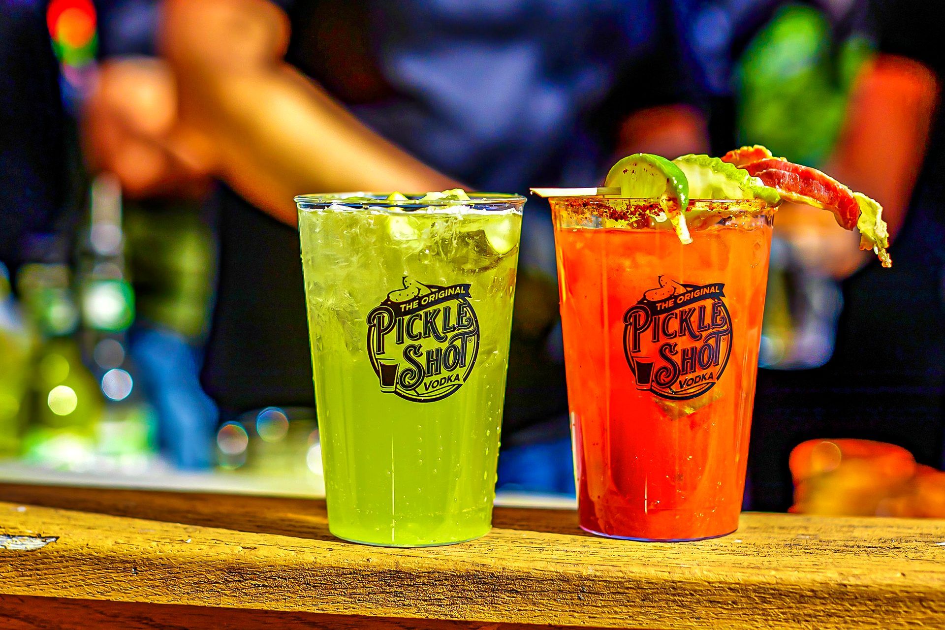 Spiked pickle lemonade and a pickle Bloody Mary garnished with crispy bacon and a fresh pickle spear, served from The Original Pickle Shot vodka activation at The Big Dill pickle festival
