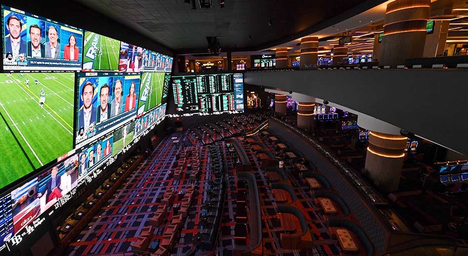 Interior of a sports betting lounge with multiple screens displaying games and odds.