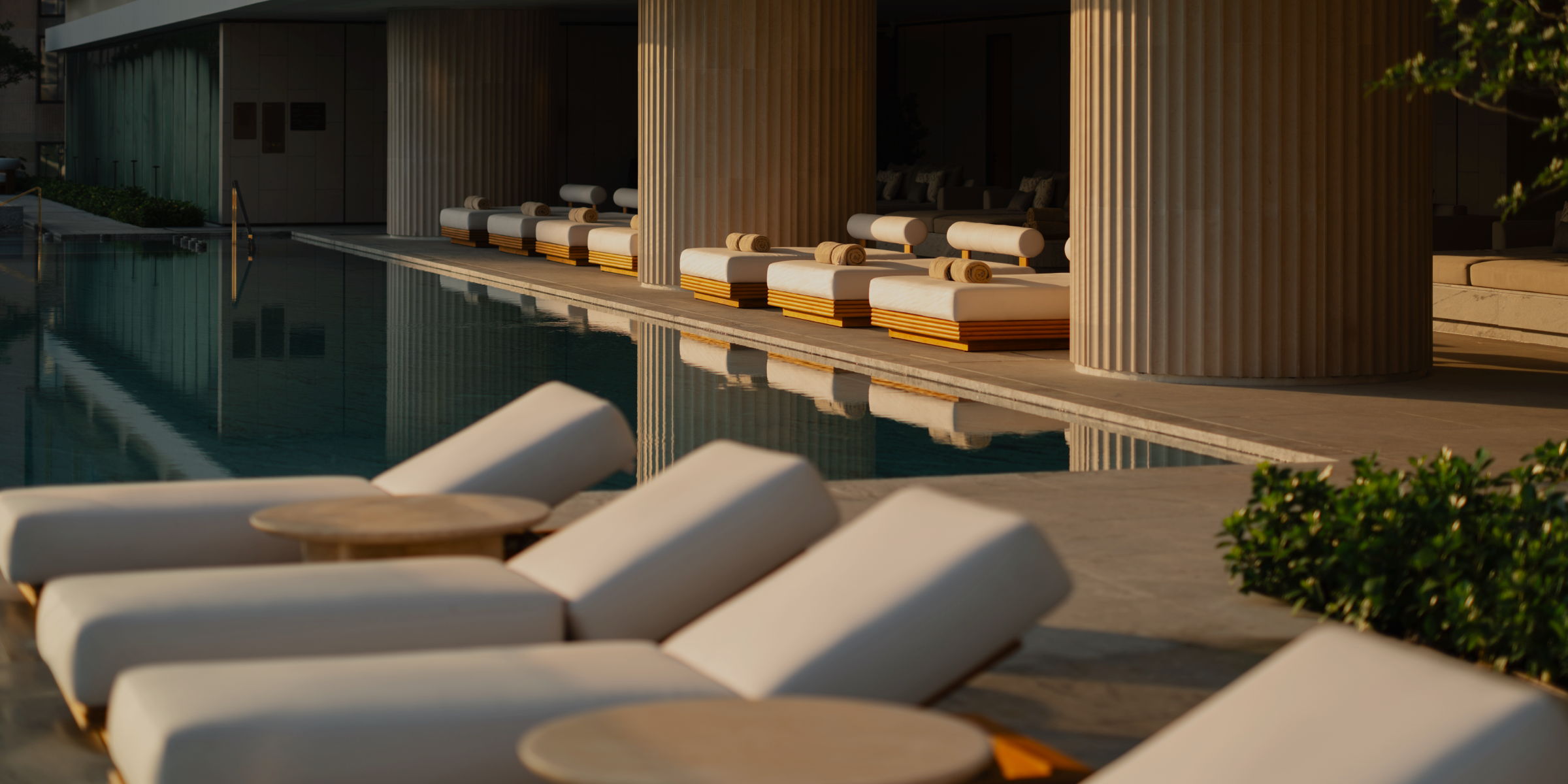 Plush white chaise loungers and daybeds in golden sunlight on the pool deck of a luxury hotel.