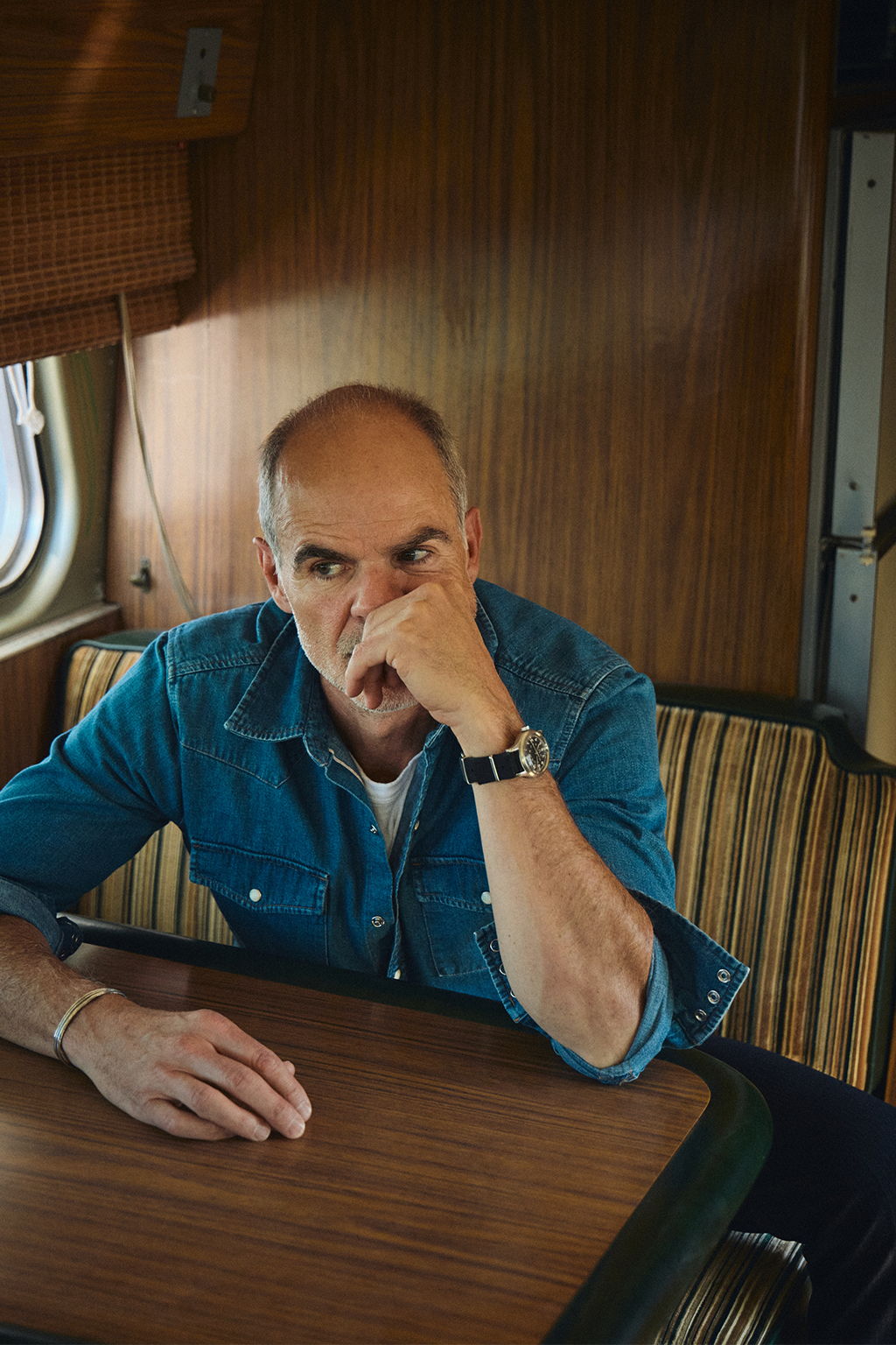 Michael Kelly inside a vintage bus in Livingston, Montana wearing the Ennis Selvedge Denim Western Shirt in Medium Wash and the Rivay Italian Wool Suit in Charcoal Herringbone Trousers