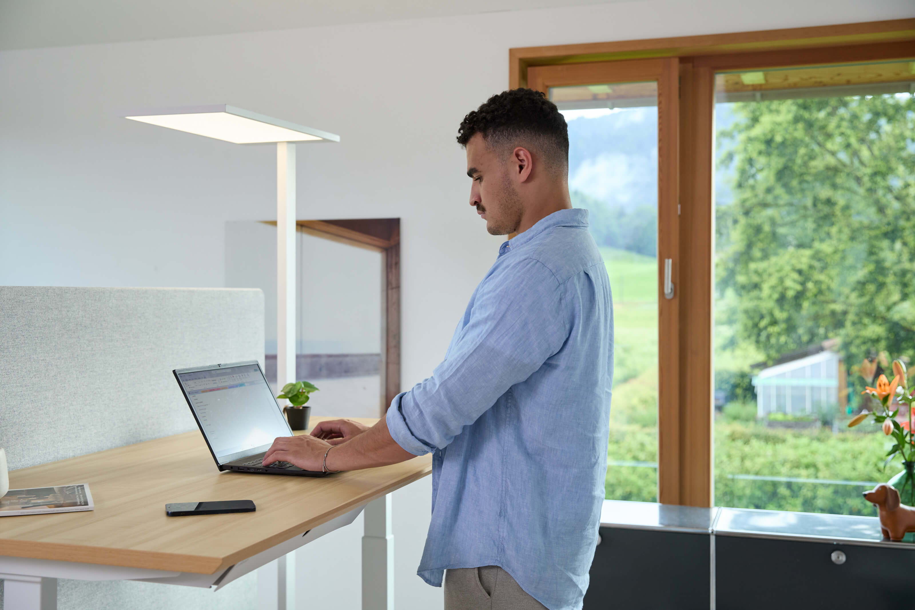 Mann arbeitet an einem ofinto Elevate mit einer Stehlampe Lumino in Weiss von ofinto, die den Arbeitsplatz perfekt beleuchtet