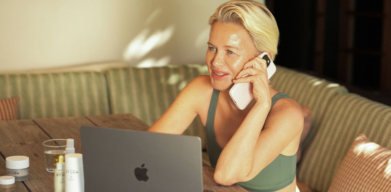 Woman talking on the phone while using a laptop at a table.