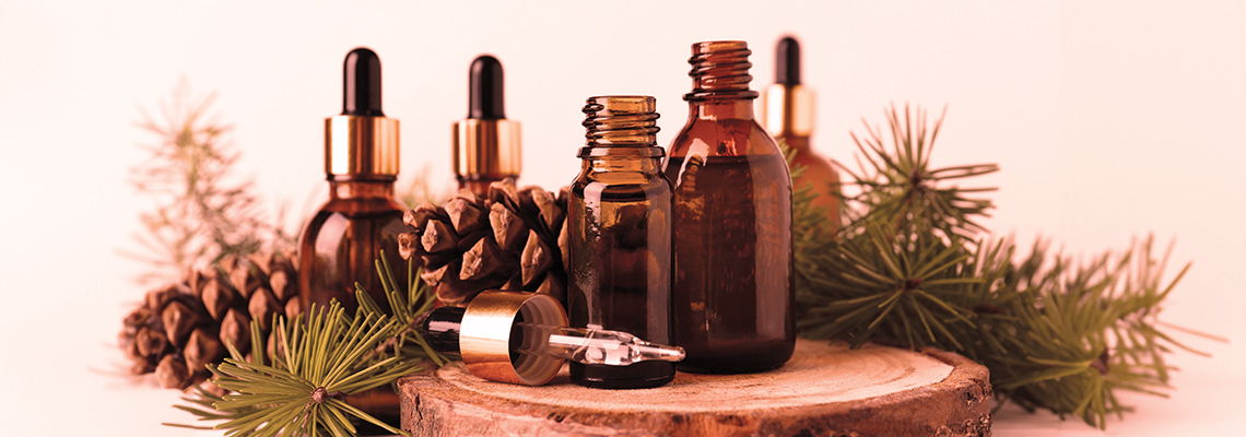 Various essential oil bottles on a wooden surface with pinecones and greenery.
