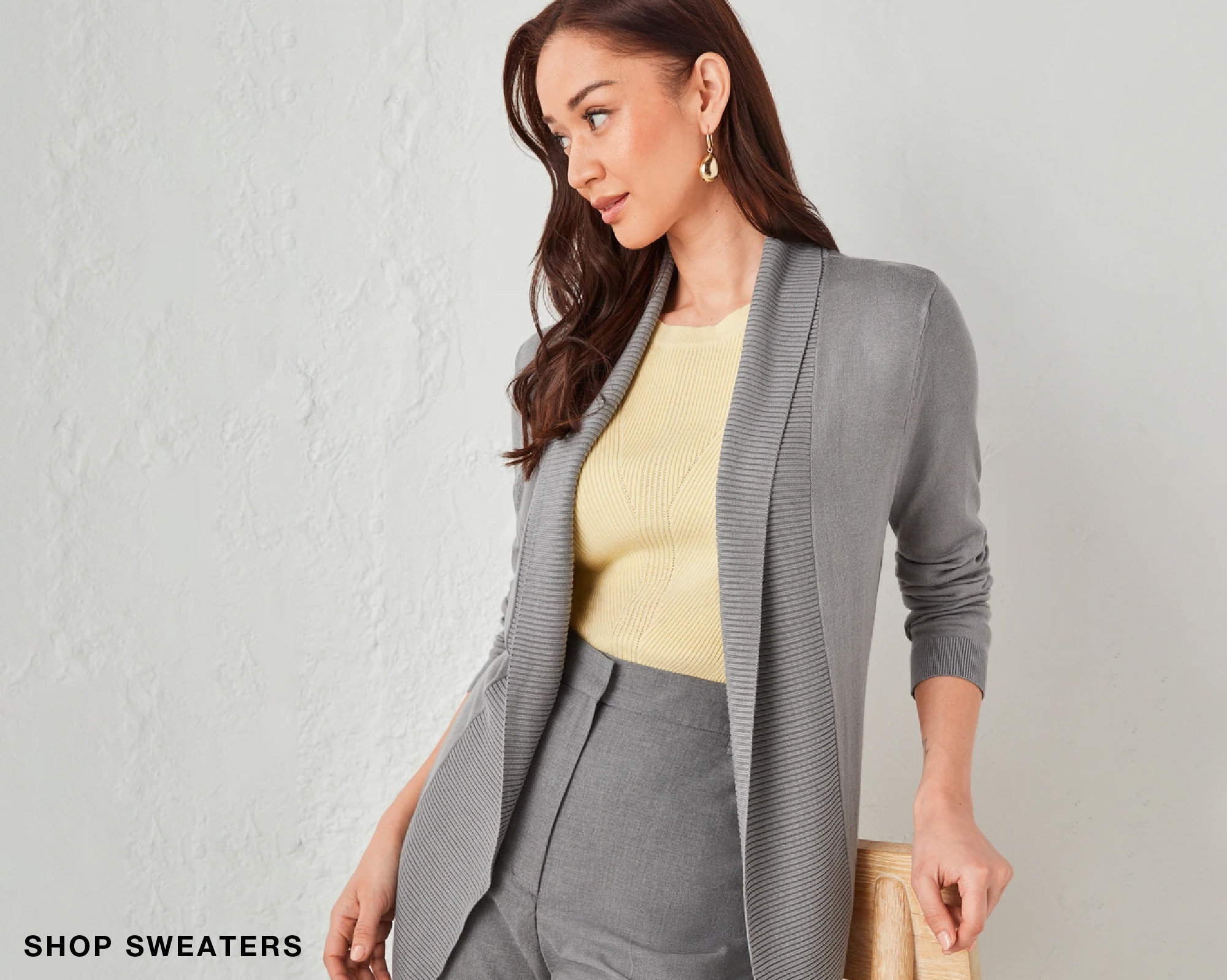 Woman in a gray cardigan with yellow top and gray pants, posing stylishly.