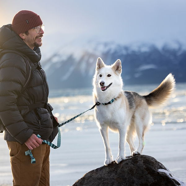 Man standing with a dog on a rock in a snowy landscape.