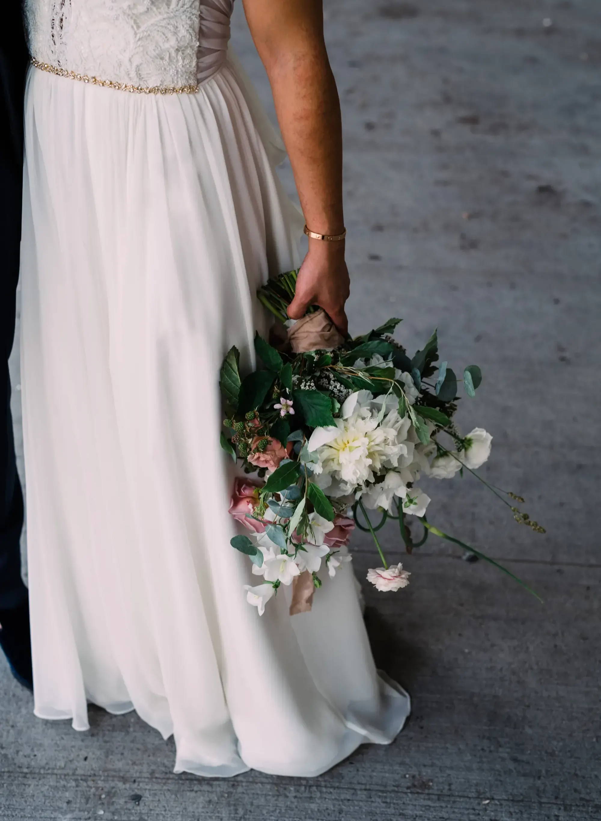 bride photographed from chest down, focused on dress resting her bridal bouquet against her dress 