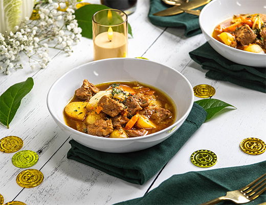A bowl of stew with vegetables and meat on a festive table setting.