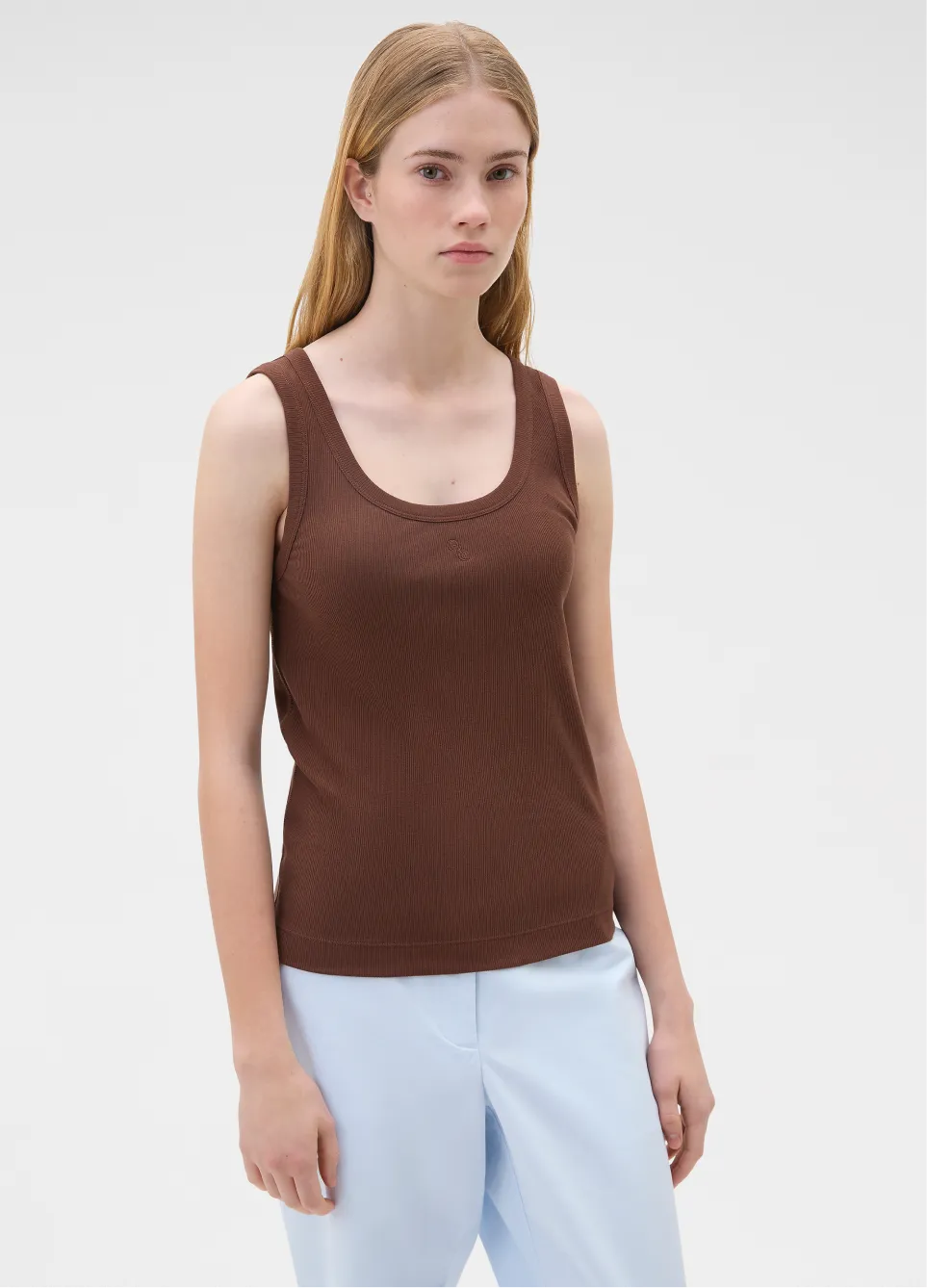 Model wearing a brown tank top and light blue pants against a plain background.