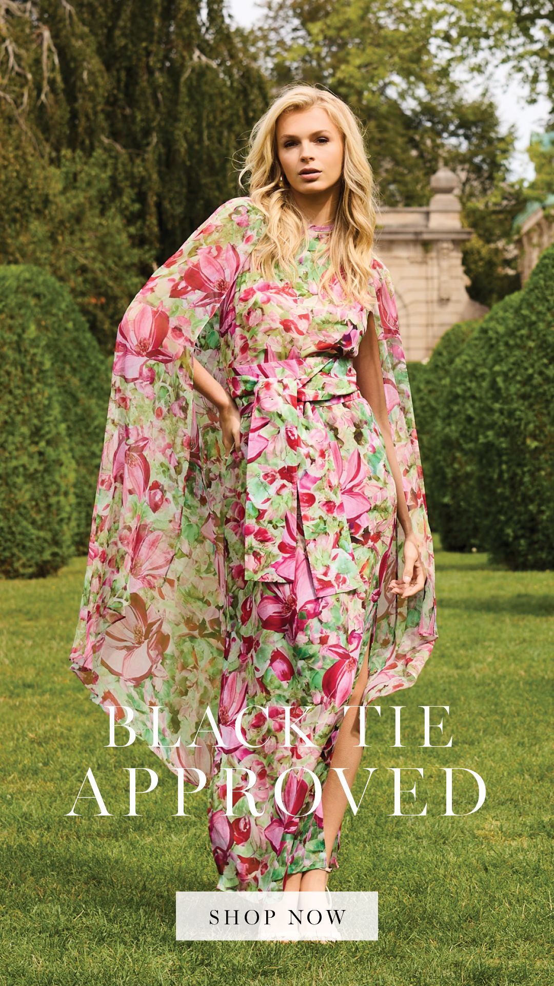 Woman in floral dress with cape in garden setting, promoting formal attire.