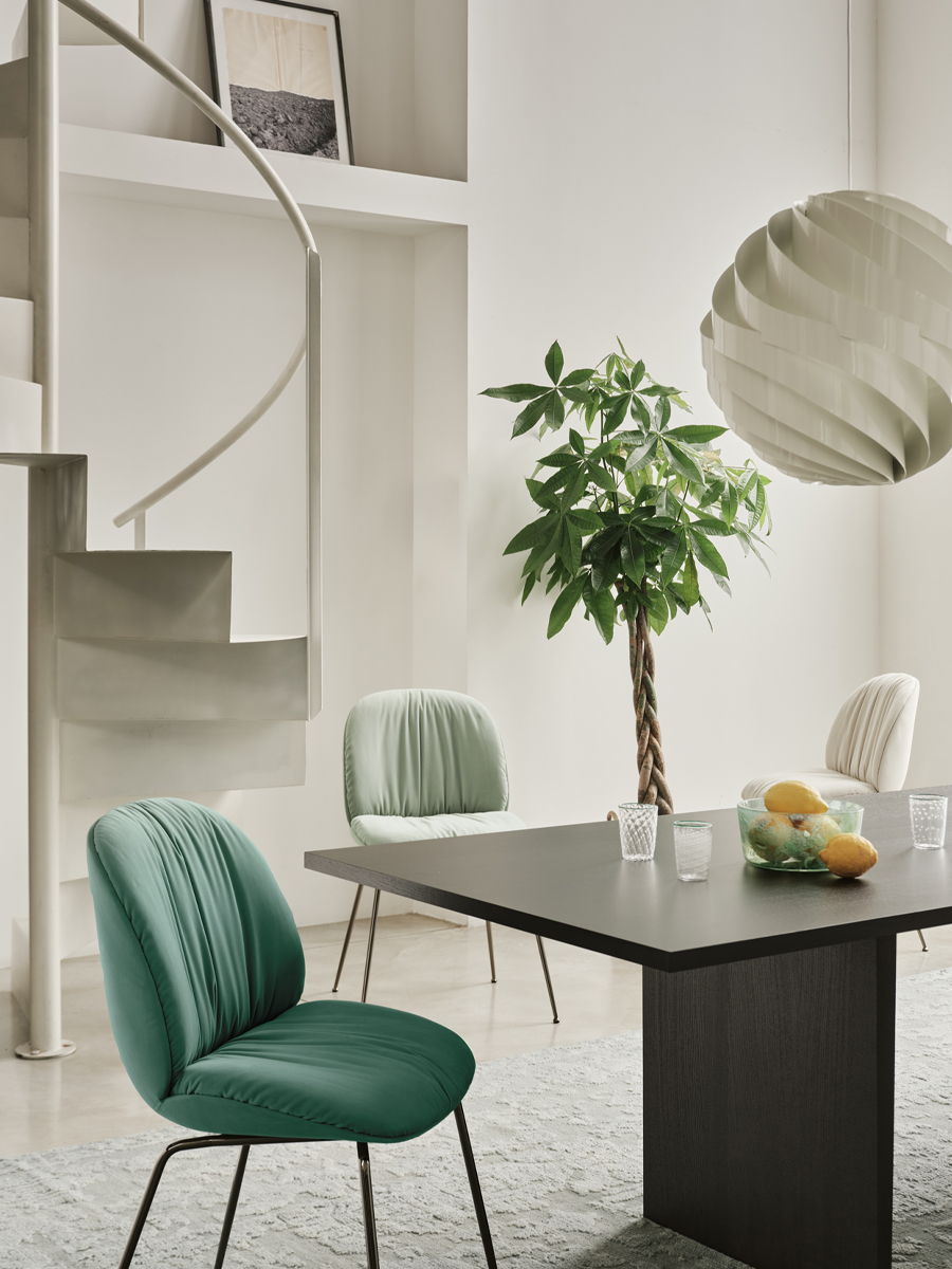 Modern GUBI dining area with a table, chairs, plant, and spiral staircase.