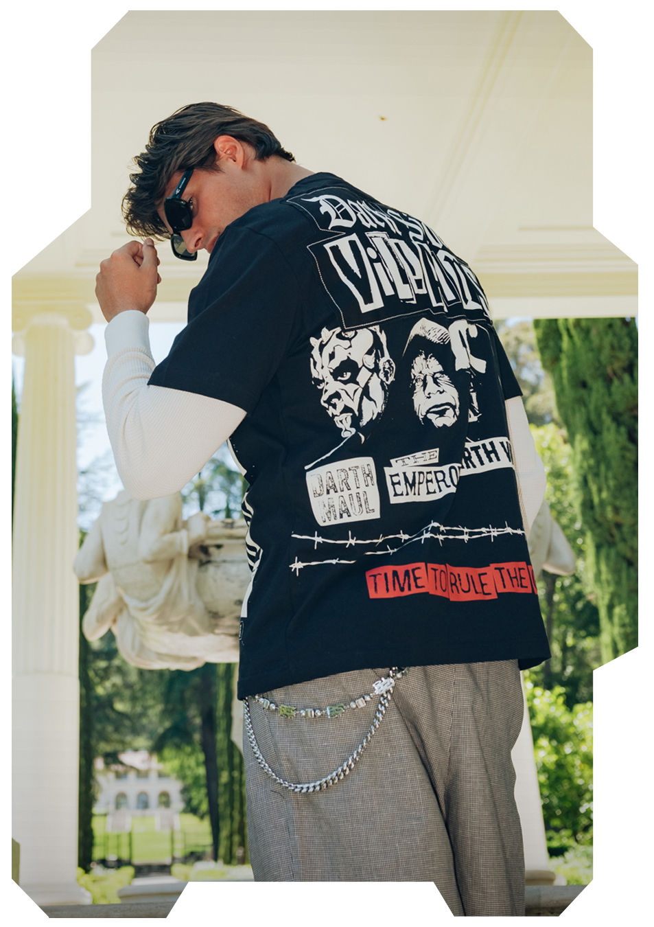 Person wearing a graphic t-shirt with chains, standing outdoors in a stylish pose.