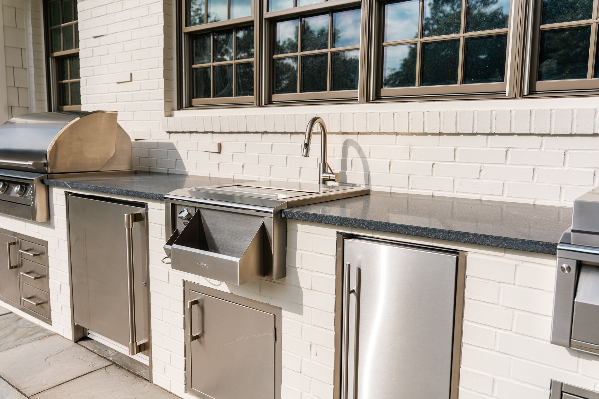 Outdoor kitchen with grill, sink, and stainless steel appliances.