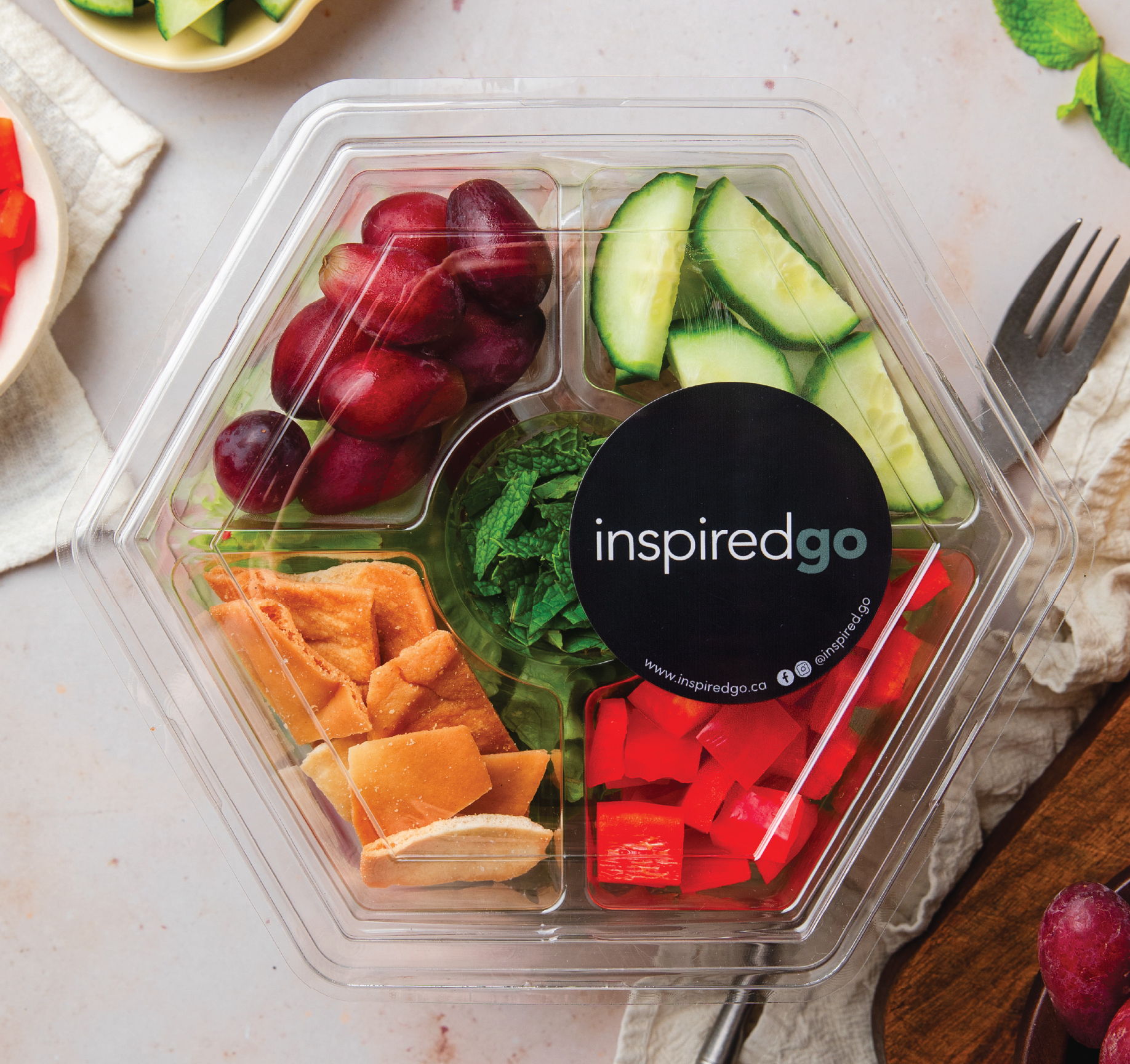 A hexagonal salad container with grapes, cucumbers, and assorted vegetables.