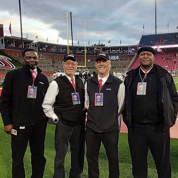 A group of bus drivers in uniform with red ties taking a picture together at a sporting event