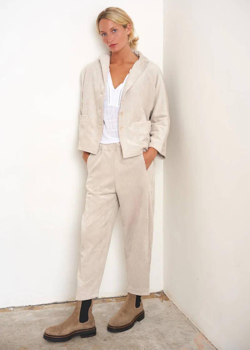 A model wearing a corduroy co-ord, oatmeal coloured jacket and trouser over a white top with chunky taupe coloured boots