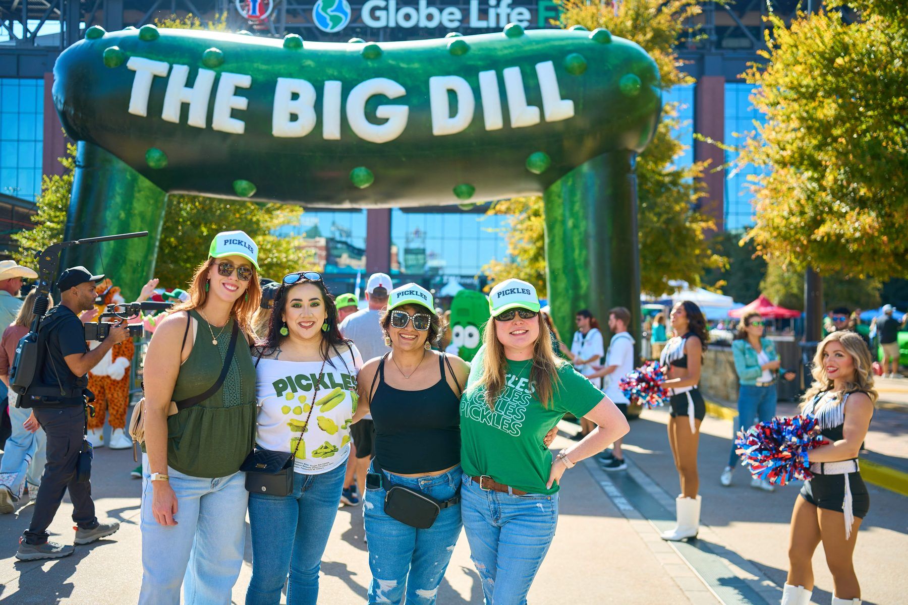 Four guests in PICKLES shirts and hats posing under The Big Dill 30-foot pickle arch at Globe Life Field in Arlington Texas 2025.