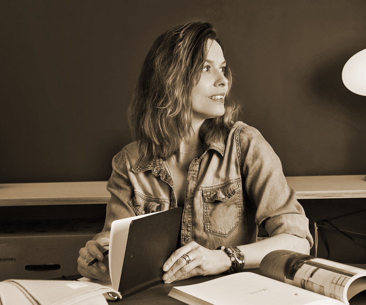 Woman sitting at a table, looking away, holding a notebook.