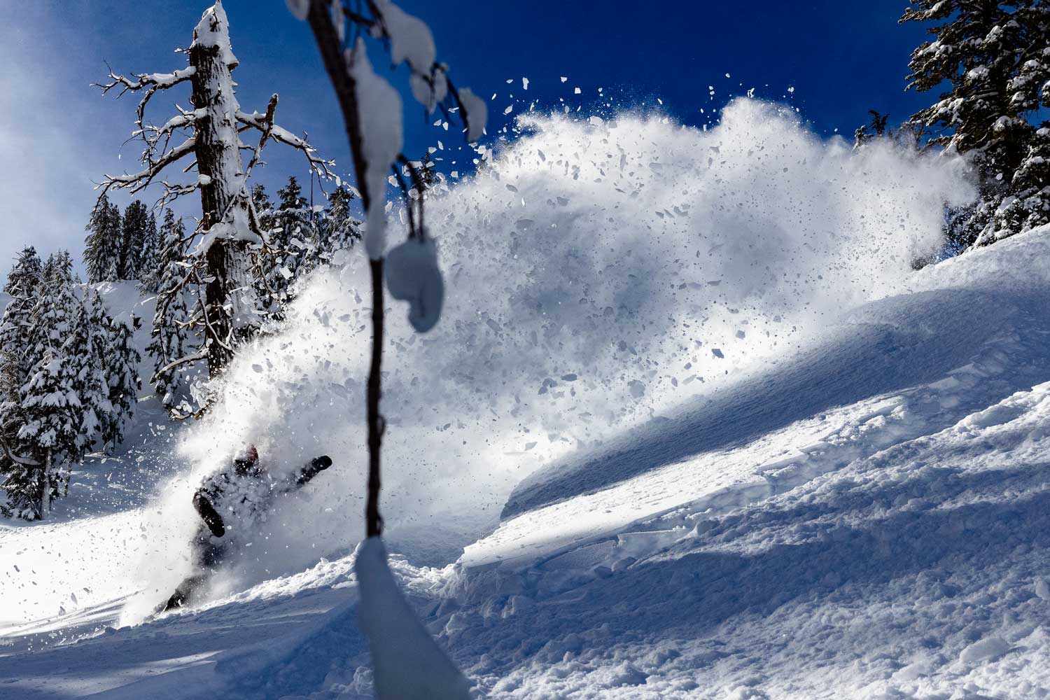 Snowboarder creating a spray of snow on a sunny mountain slope.