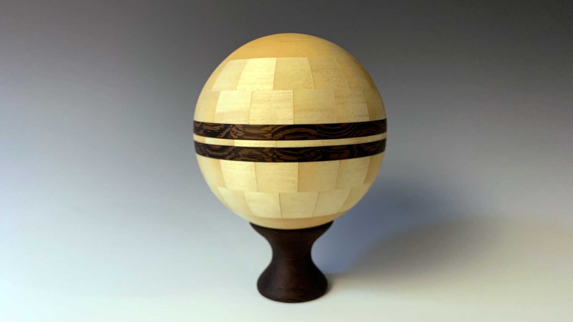 A wooden globe sculpture with a pedestal base, featuring light and dark wood patterns.