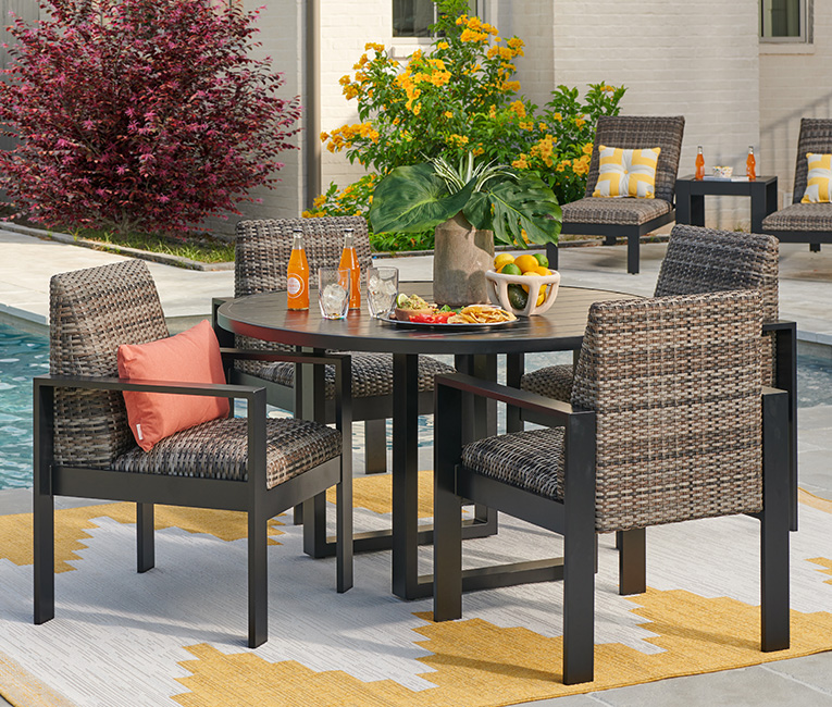 Outdoor dining set with four chairs around a table by a pool.